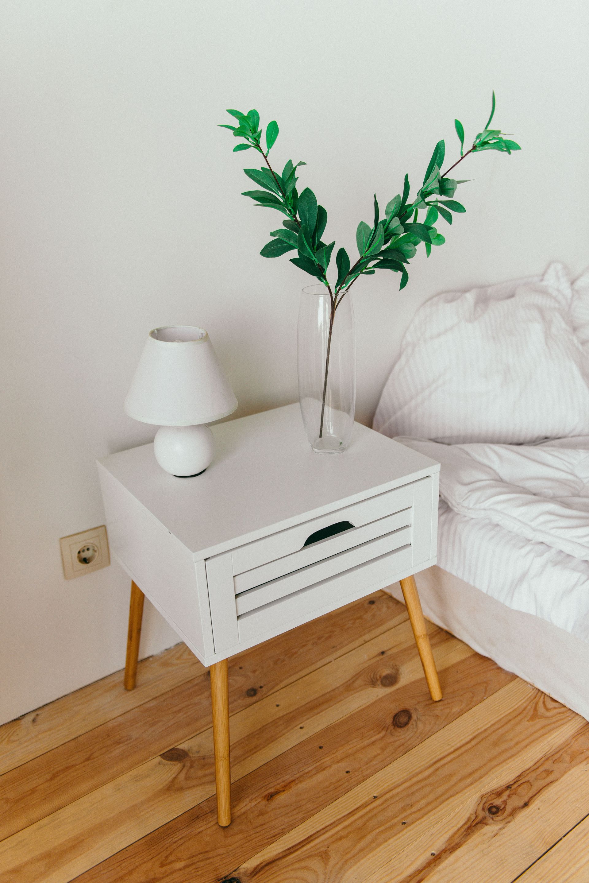 A stylish bedroom showcasing a white nightstand with a vase and lamp, perfect for modern interior design inspiration.